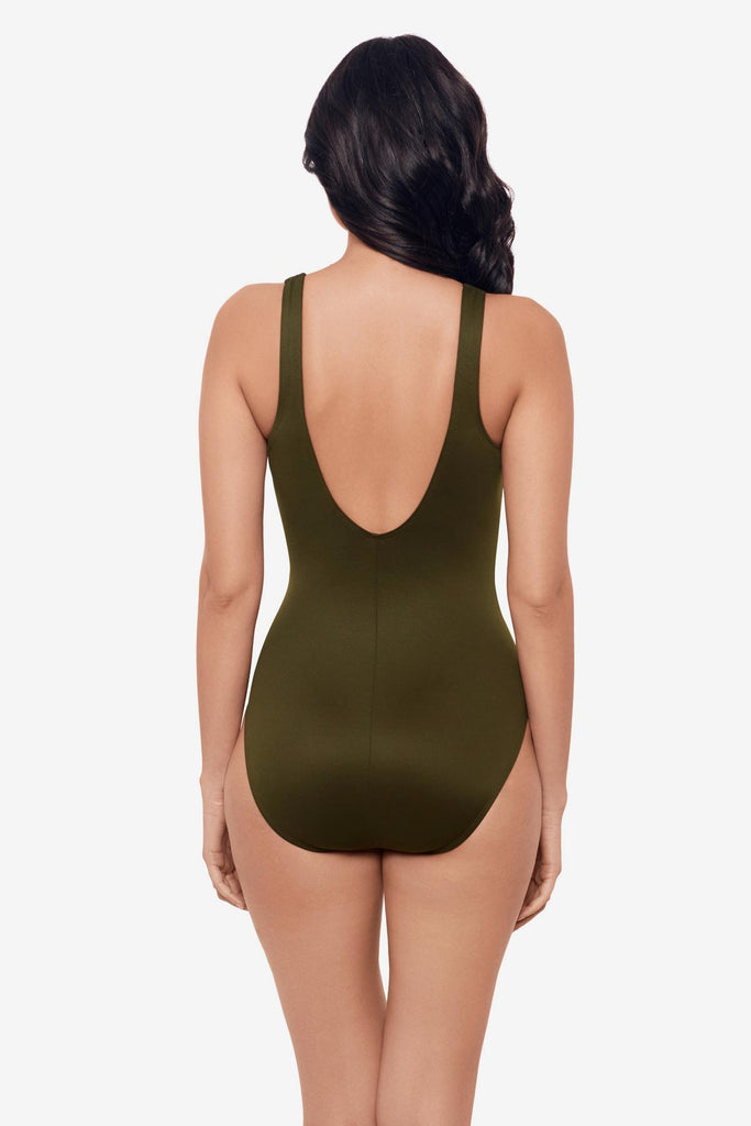 Woman facing away wearing a nori green one-piece swimsuit with a mesh cut out on the left side 