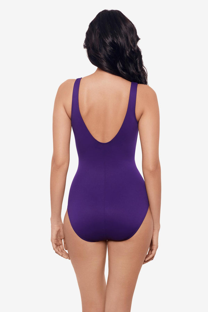 Woman facing away wearing a mulberry purple one-piece swimsuit with ruching on the side