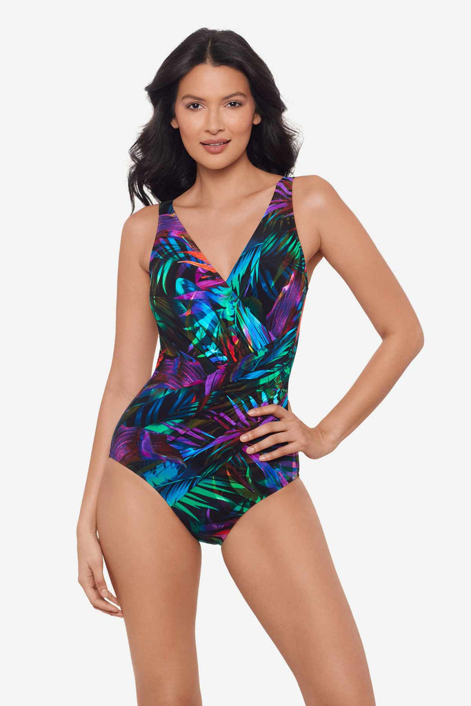 Woman with hand on hip wearing a multicolor one-piece swimsuit with neon palm leaves