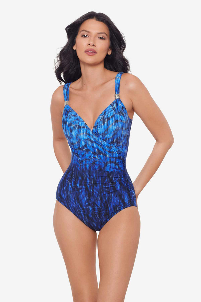 Woman with hands behind back wearing a black and blue one-piece swimsuit with details on the straps