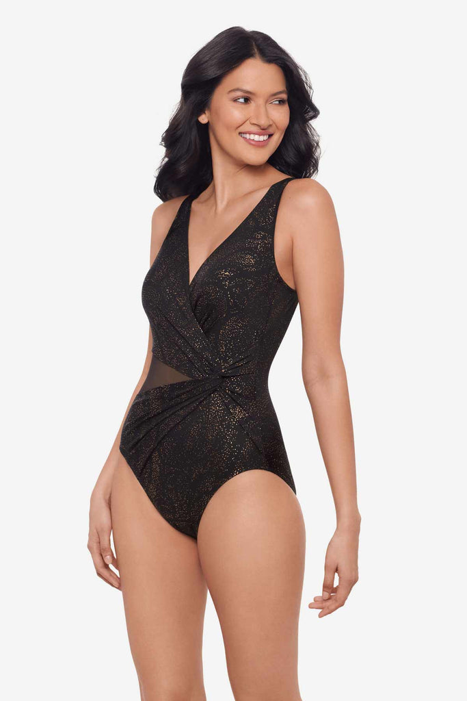 Woman wearing a black shimmery one-piece swimsuit with mesh cut out on left side while looking right