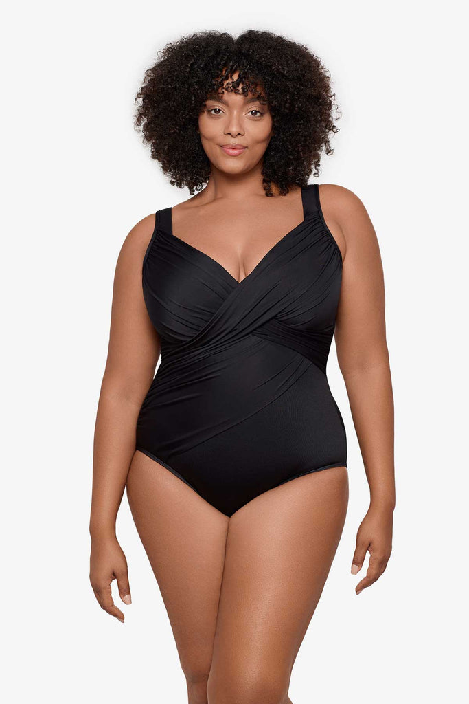 Woman wearing a black one-piece swimsuit with wrap detail on the front