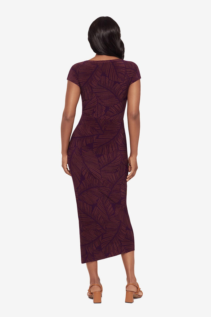 Woman turned away wearing a purple dress with a palm leaf print