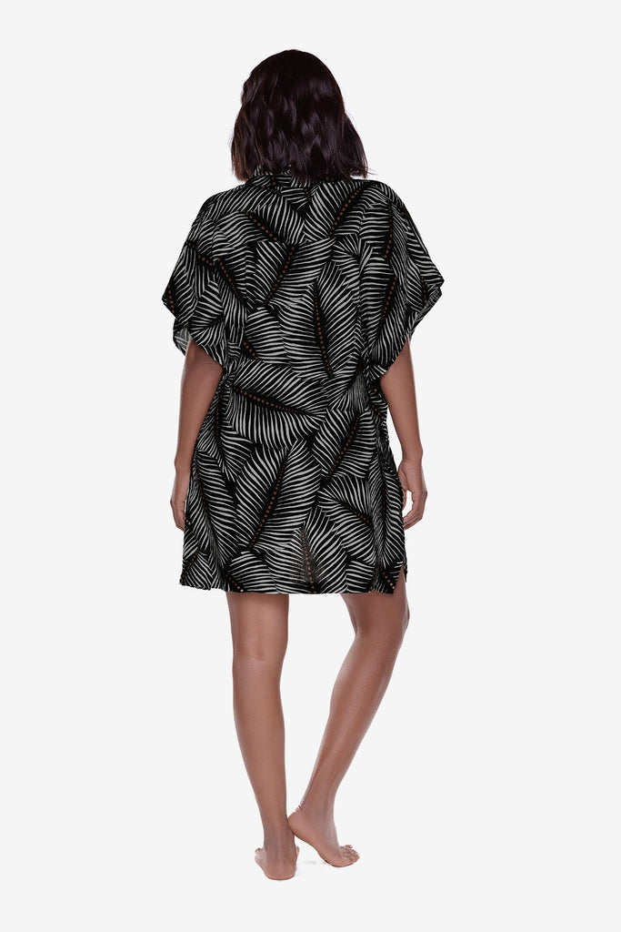 Woman turned away wearing an oversized swim shirt cover up with a black and white leaf print