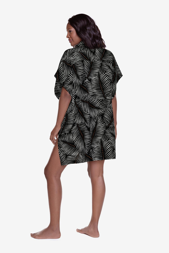 Woman turned left wearing an oversized swim shirt cover up with a black and white leaf print