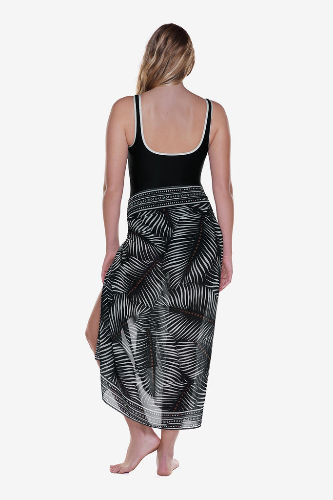 Woman turned away wearing a swim cover up around the waist with a palm leaf print