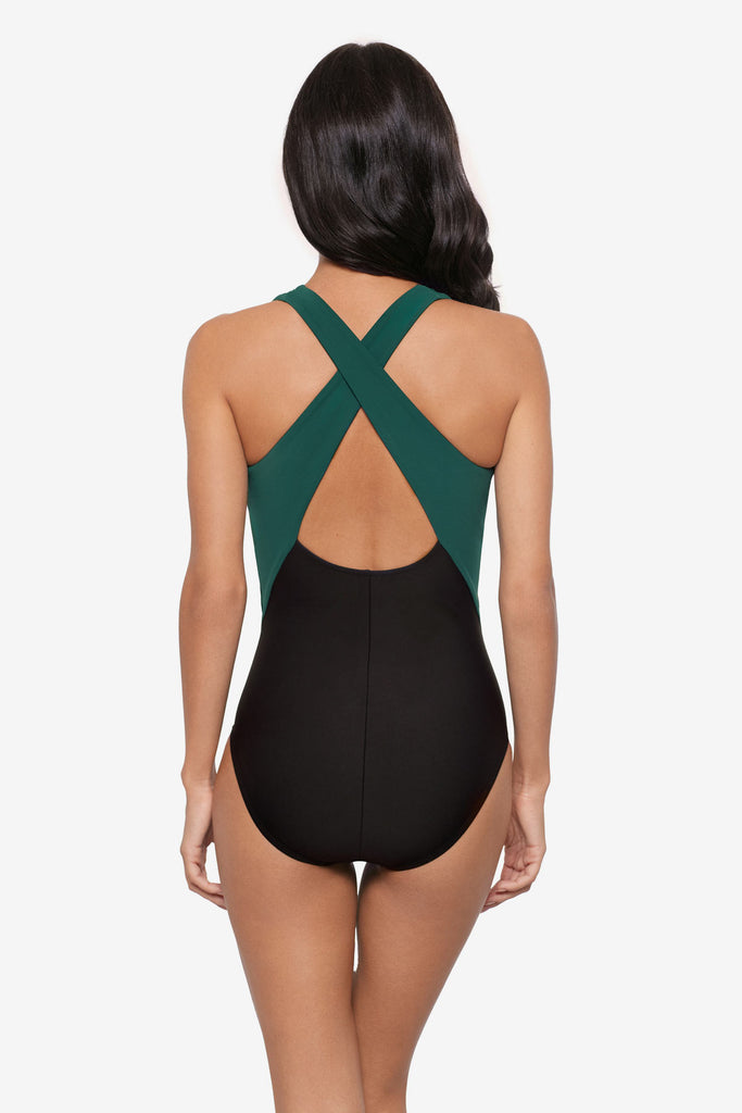 Woman turned away wearing a green and black one-piece swimsuit with an X back